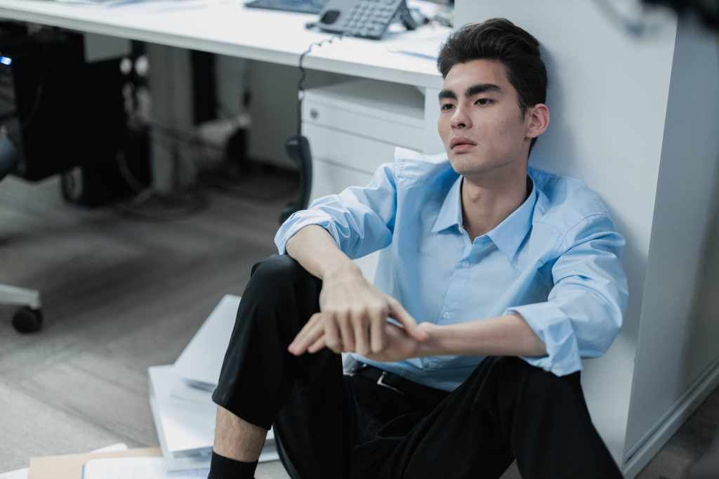 Exhausted Asian office worker sitting on the floor, reflecting burnout, stress and emotional emptiness at work.