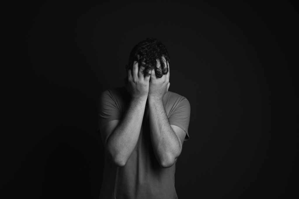 Person covering their face in a dark setting, symbolising anxiety, mental pain and inner suffering.